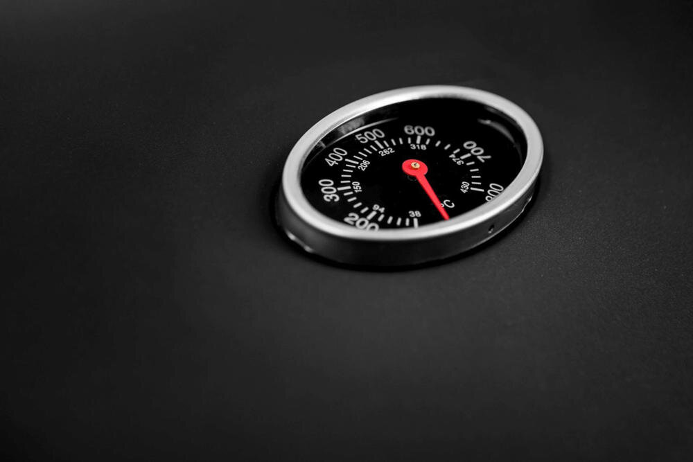 Na czarnym tle znajduje się okrągły termometr z czerwoną wskazówką, pokazujący temperaturę w stopniach Celsjusza od 0 do 600.