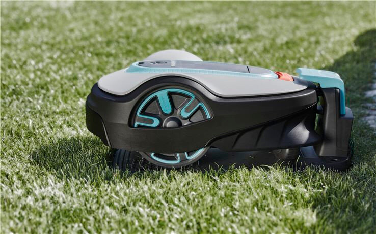 Robot koszący na trawie, z widocznymi elementami w kolorze czarnym i turkusowym. Na obudowie znajduje się logo \'GARDENA\'.