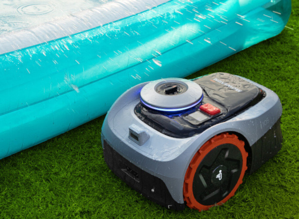 Robot koszący na trawie obok niebieskiego basenu, z widocznymi kroplami wody na obudowie. Na robocie widoczne są przyciski i logo producenta.