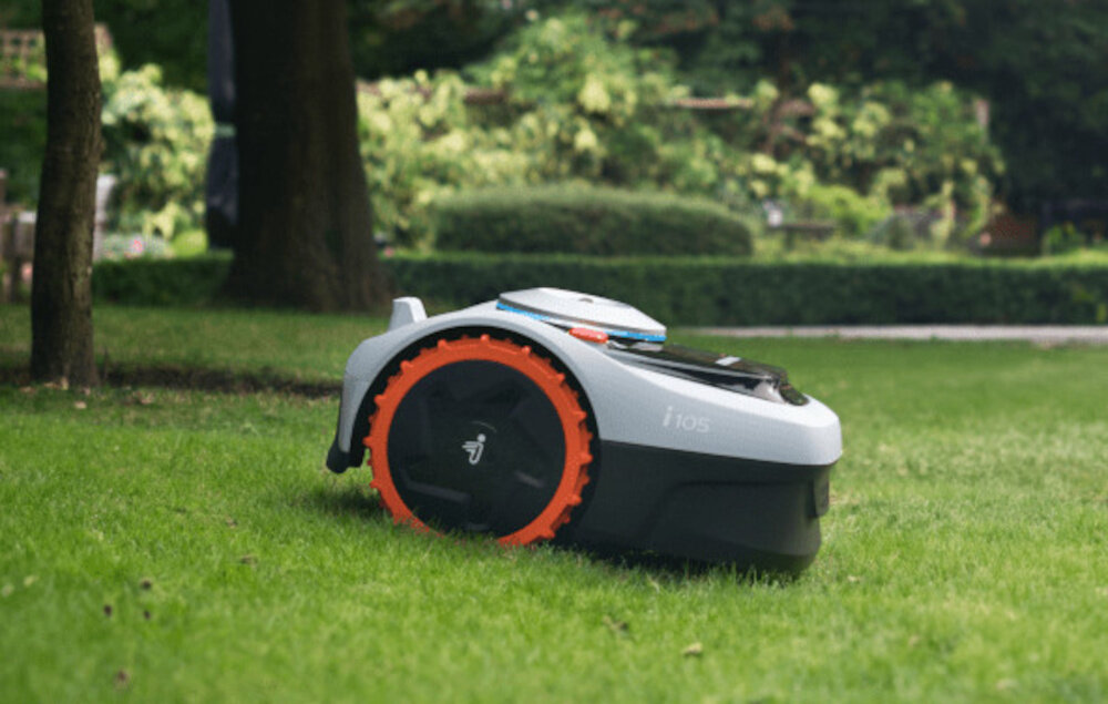 Robot koszący na trawie, z widocznym napisem \'i105\' na boku. W tle znajdują się drzewa i krzewy.
