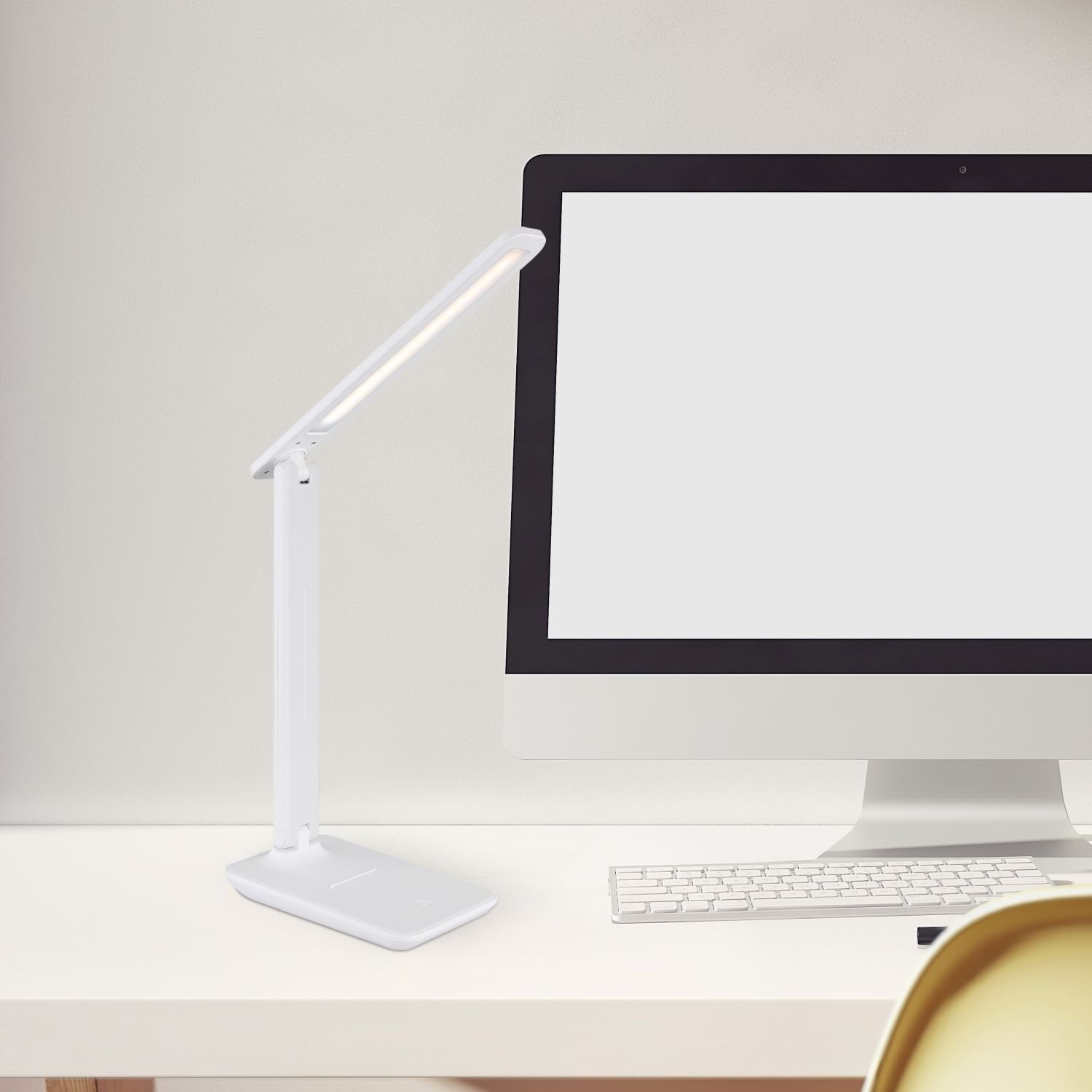 Na biurku stoi biała lampa biurkowa LED obok monitora i klawiatury. Lampa ma smukły, nowoczesny design.