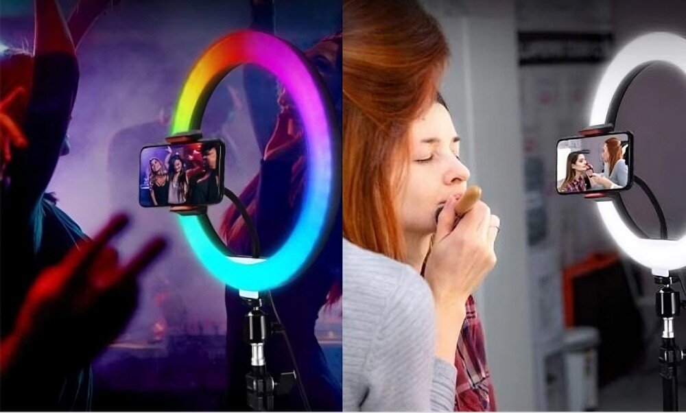 Obraz przedstawia lampę pierścieniową z uchwytem na telefon, emitującą kolorowe światło RGB po lewej stronie i białe światło po prawej stronie. W tle widoczne są osoby korzystające z lampy.