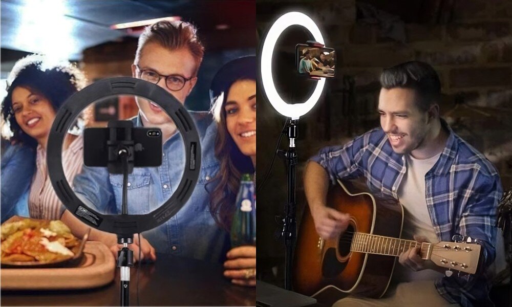 Na obrazie widać lampę pierścieniową ustawioną na statywie, z zamocowanym smartfonem. W tle znajdują się osoby oraz mężczyzna grający na gitarze.