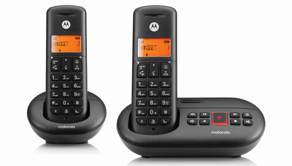 Dwa czarne telefony bezprzewodowe z pomarańczowymi wyświetlaczami, na których widoczny jest tekst \'PROSZĘ\'. Oba telefony mają logo \'M\' oraz klawiaturę numeryczną, a jeden z nich jest umieszczony na bazie z przyciskami sterującymi.