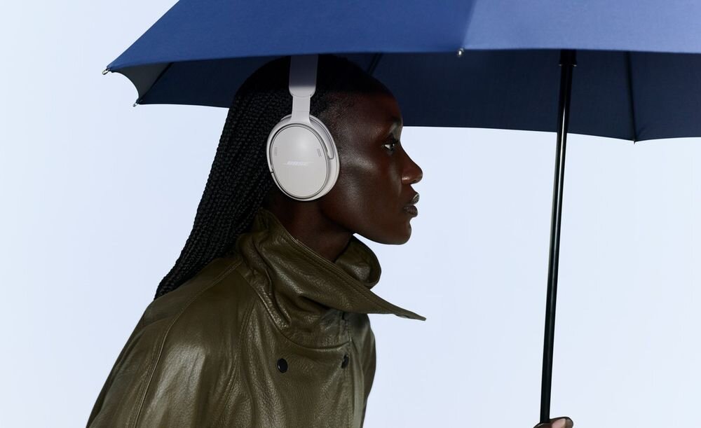 Słuchawki nauszne BOSE QuietComfort 2ND Gen ANC w kolorach czarnym, białym, eukaliptusowej zieleni, palisandrowej malwie i mięcie, osoba z założonymi słuchawkami pod parasolką
