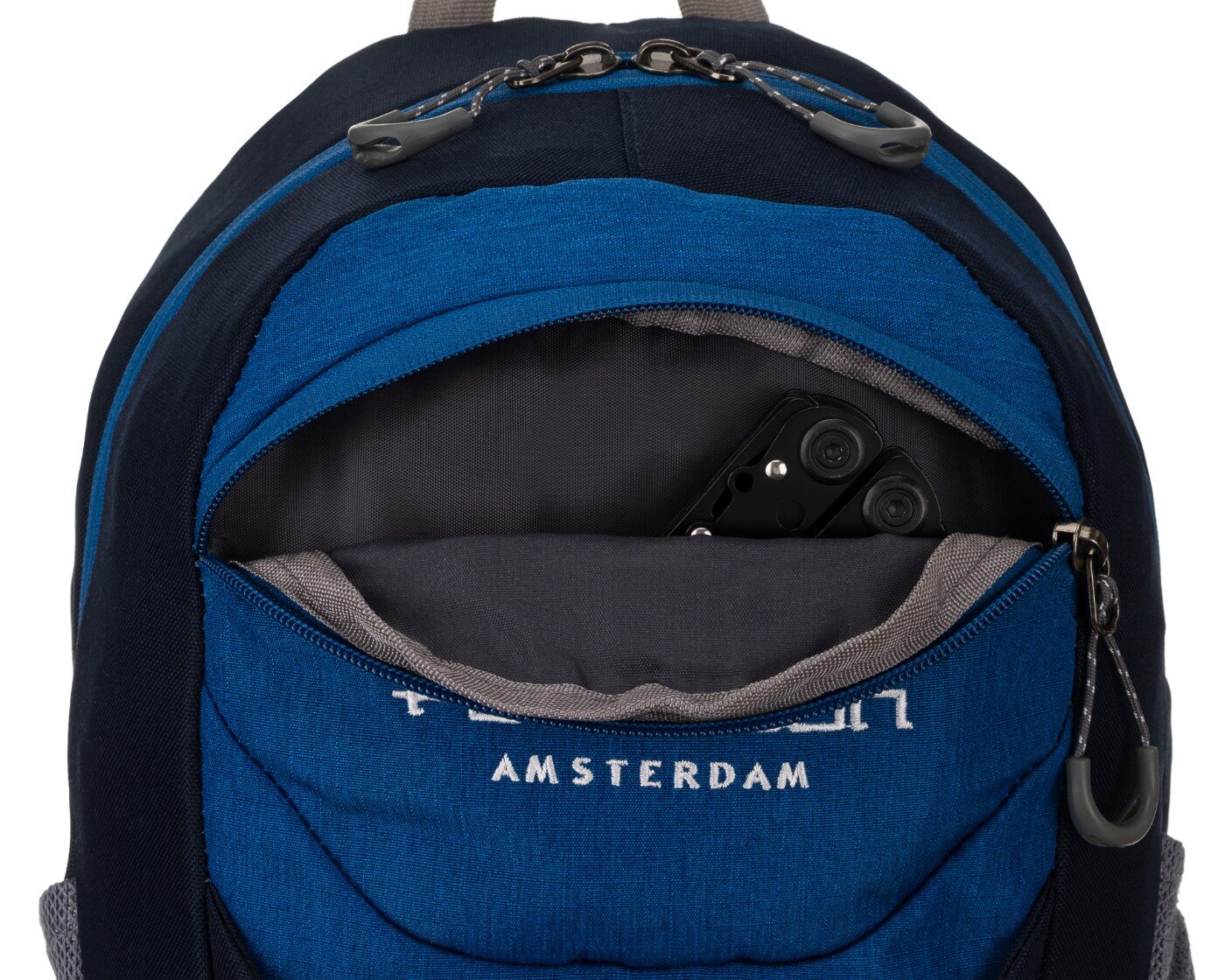 Granatowy plecak z widoczną kieszenią, w której znajduje się czarny przedmiot. Na kieszeni widoczny jest napis \'AMSTERDAM\'.