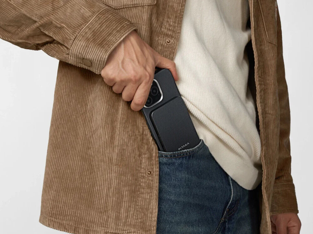 Osoba wkłada czarno-szary powerbank z napisem \'PITAKA\' do kieszeni spodni. Powerbank ma teksturowaną powierzchnię i jest trzymany w dłoni.