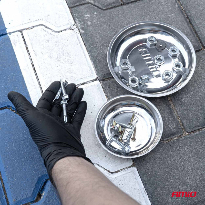 Na obrazie widoczne są dwie metalowe miski magnetyczne z różnymi śrubami i nakrętkami, a obok ręka w czarnej rękawiczce trzymająca śruby. Na jednej z misek widnieje logo \'AMiO\'.