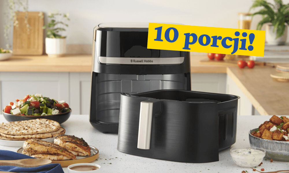 Na blacie kuchennym stoi czarna frytkownica beztłuszczowa z logo \'Russell Hobbs\', obok niej znajduje się wyjmowany kosz. Na żółtym tle widnieje napis \'10 porcji!\'.