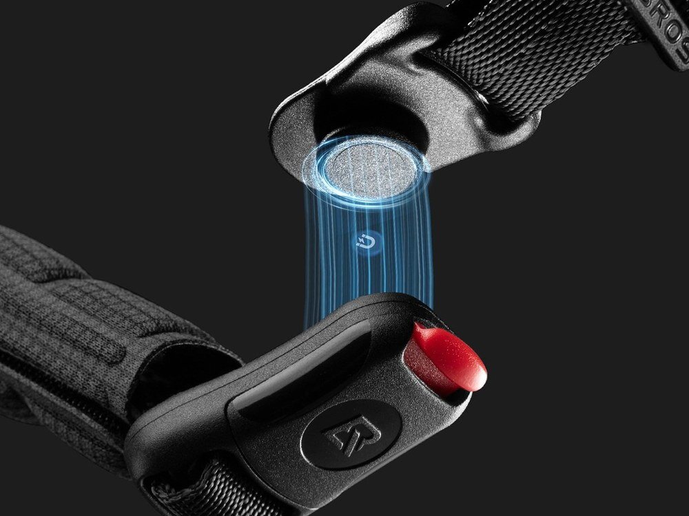 Zbliżenie na zapięcie kasku rowerowego z magnetycznym mechanizmem, z widocznym niebieskim efektem świetlnym. Na zapięciu znajduje się czerwony przycisk oraz logo w kształcie litery \'R\'.