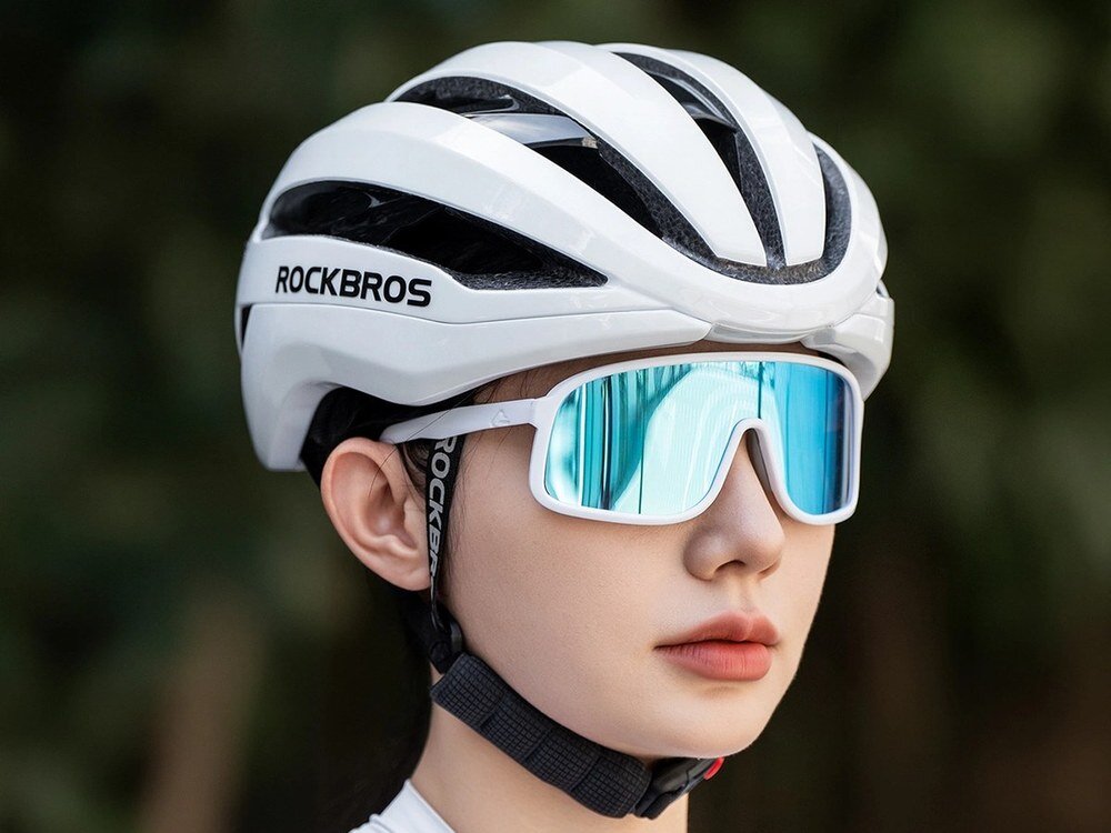 Osoba nosi biały kask rowerowy z napisem ROCKBROS oraz okulary przeciwsłoneczne z niebieskimi szkłami.