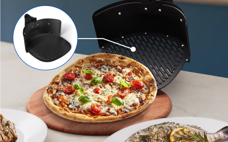 Na obrazie widoczna jest pizza z pomidorami i bazylią na drewnianej desce oraz grillowana ryba na talerzu. Wstawka pokazuje czarną, okrągłą kratkę, prawdopodobnie element frytkownicy beztłuszczowej.