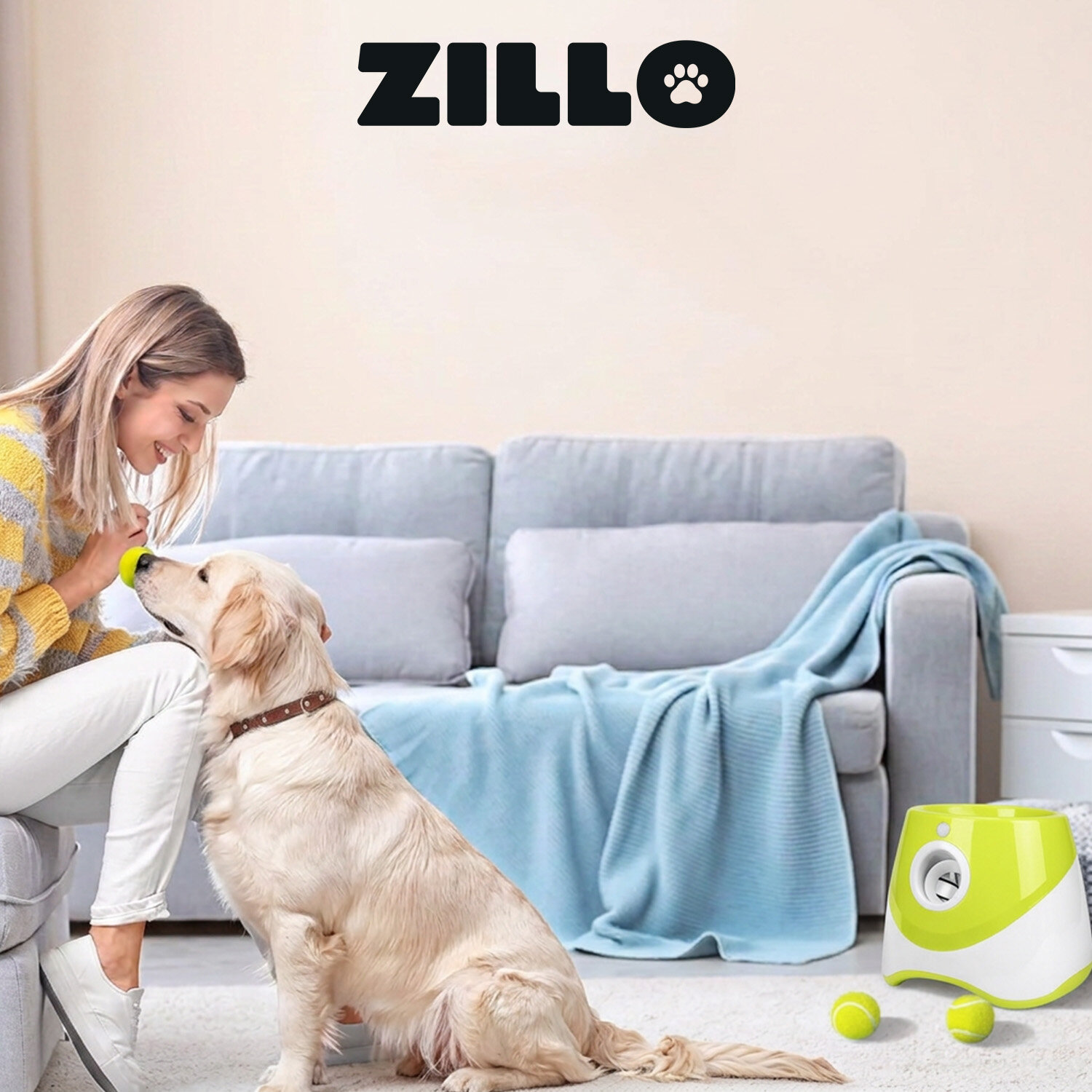 Na obrazie widać kobietę siedzącą na kanapie, trzymającą piłkę przed psem. Obok kanapy znajduje się żółta wyrzutnia piłek z logo \'ZILLO\'.