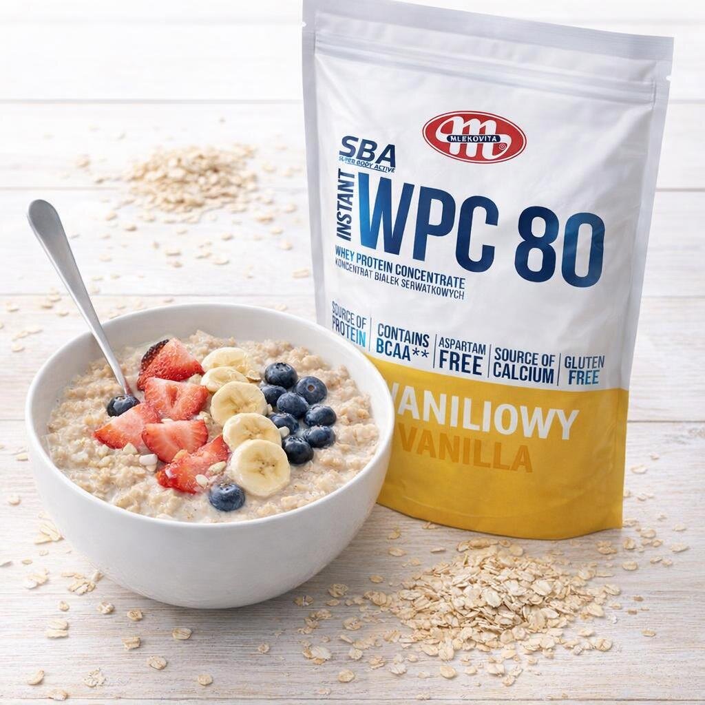 Na obrazie widoczna jest miska owsianki z plasterkami bananów, truskawkami i borówkami oraz opakowanie produktu z napisem \'Mlekovita SBA Instant WPC 80 Whey Protein Concentrate Koncentrat Białek Serwatkowych Waniliowy Vanilla\'.