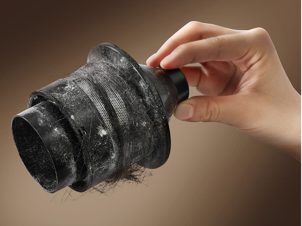 Osoba trzyma w ręku czarny filtr odkurzacza pokryty kurzem i włosami.