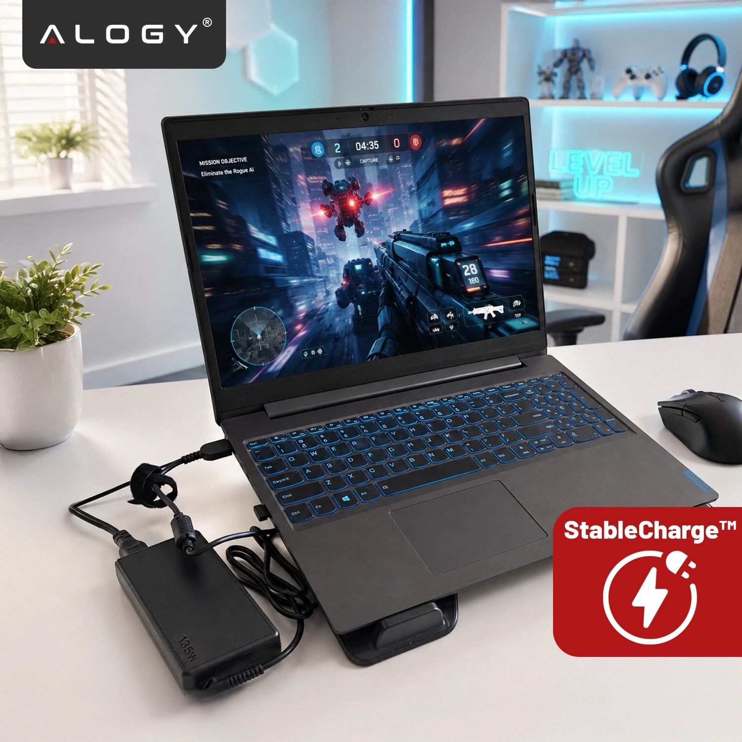 Na biurku znajduje się laptop z włączoną grą, podłączony do zasilacza oznaczonego jako 135W. W rogu widoczne jest logo \'Alogy\' oraz symbol \'StableCharge™\'.