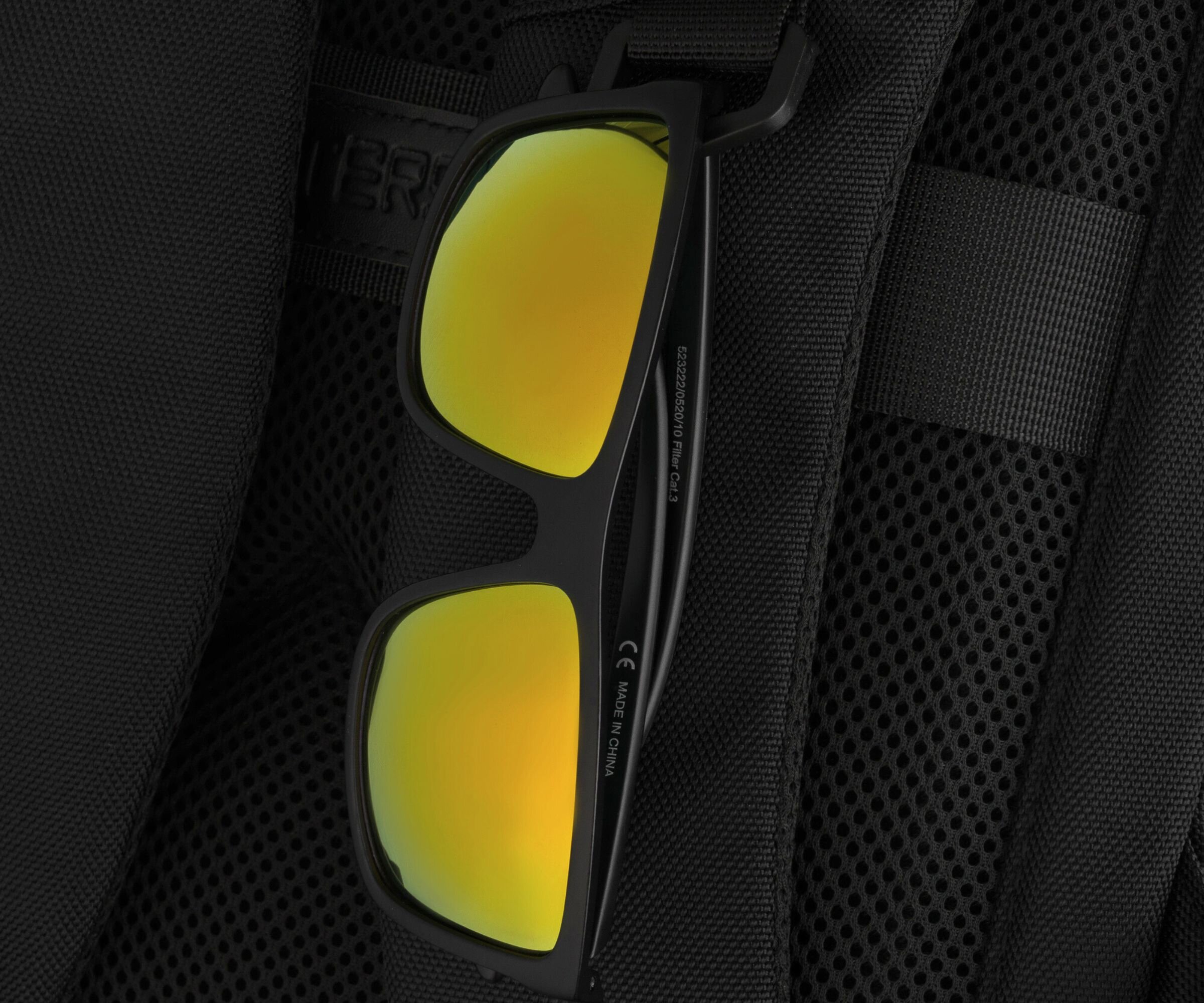 Czarne okulary przeciwsłoneczne z żółtymi soczewkami są umieszczone na czarnym plecaku z siateczkowym materiałem. Na zauszniku okularów widoczny jest napis \'MADE IN CHINA\'.