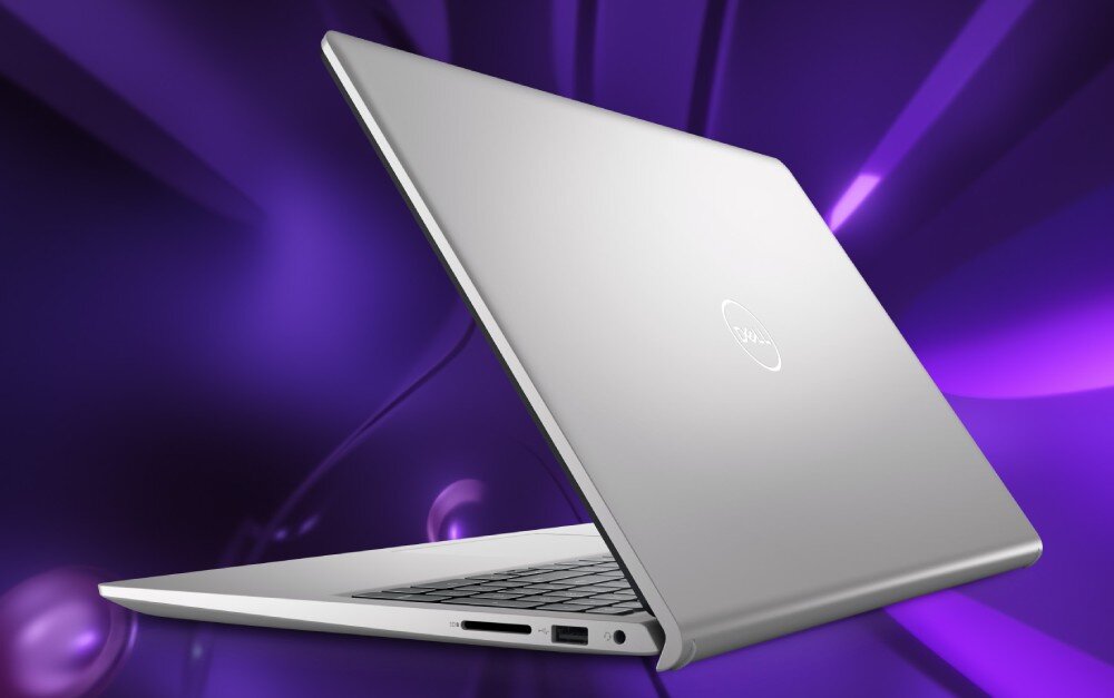 Srebrny laptop z logo Dell na pokrywie, ustawiony pod kątem na tle fioletowych, abstrakcyjnych kształtów. Widoczne są porty po jednej stronie urządzenia.