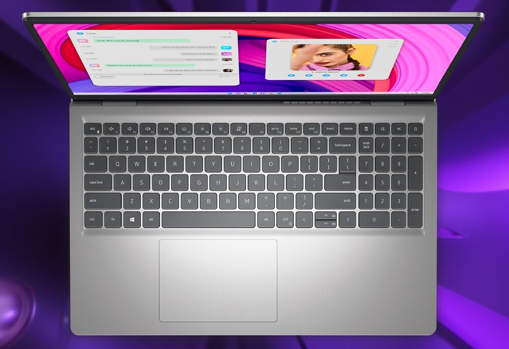 Laptop z widoczną klawiaturą i touchpadem, na ekranie wyświetlane są aplikacje z wiadomościami i zdjęciem. Tło jest fioletowe z abstrakcyjnymi wzorami.