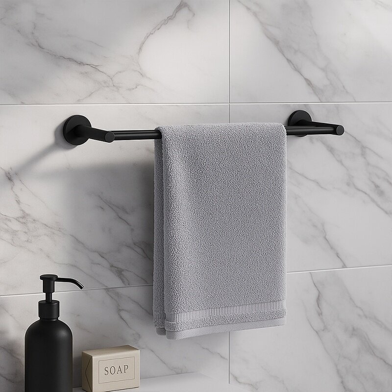 Na ścianie z marmurowymi płytkami zamontowany jest czarny wieszak łazienkowy z szarym ręcznikiem. Obok znajduje się czarny dozownik na mydło i pudełko z napisem \'SOAP\'.