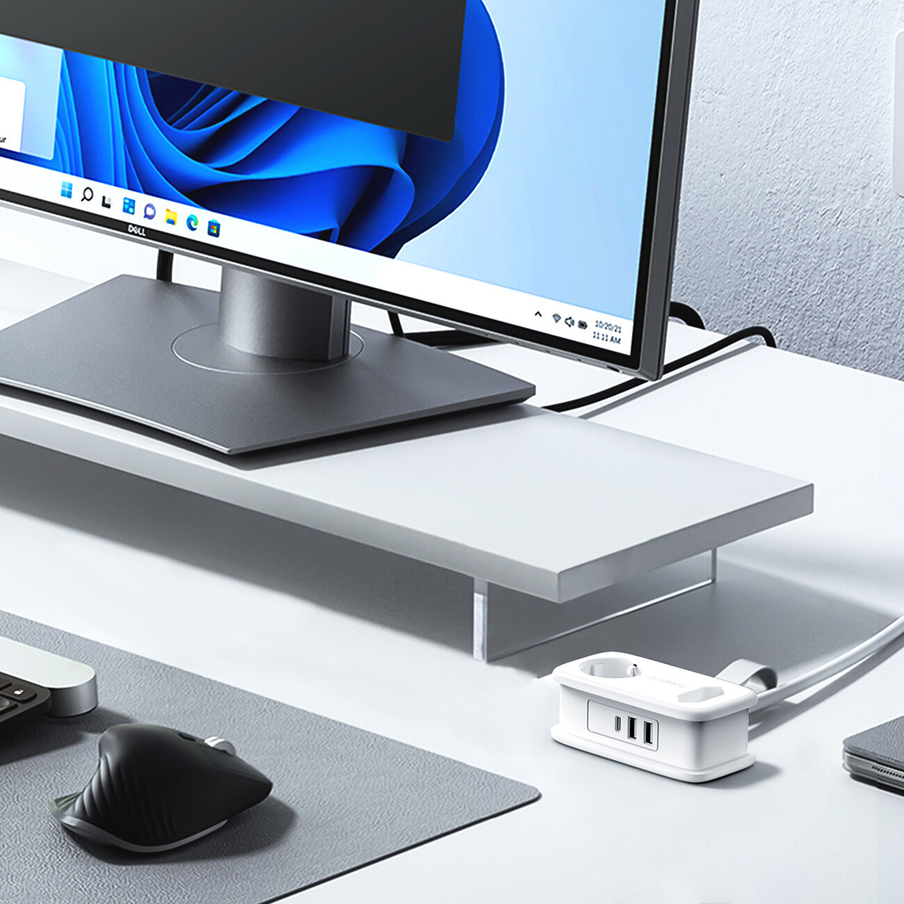 Na biurku znajduje się monitor na podstawce, a obok niego biała listwa zasilająca z dwoma gniazdami AC, dwoma portami USB-A i jednym portem USB-C. W tle widać fragment klawiatury i myszki na podkładce.