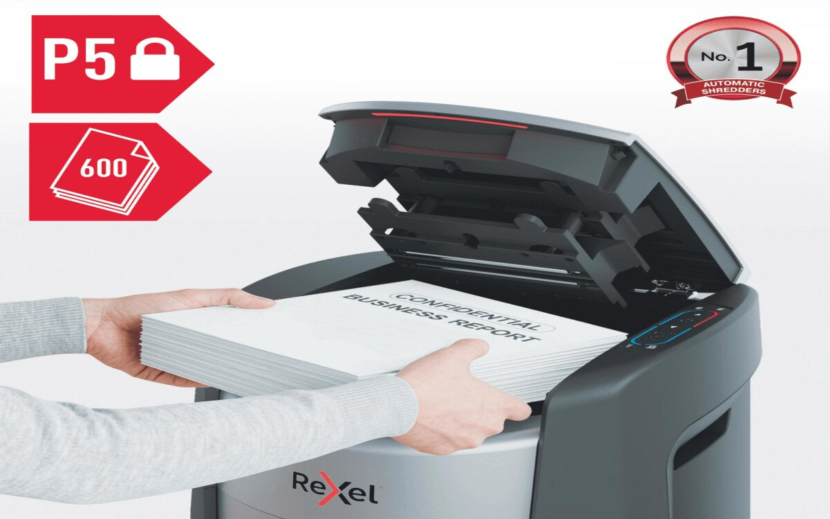 Niszczarka z otwartą pokrywą, do której wkładane są dokumenty z napisem 'CONFIDENTIAL BUSINESS REPORT'. Widoczne logo Rexel oraz oznaczenia P5 i 600 na czerwonym tle.