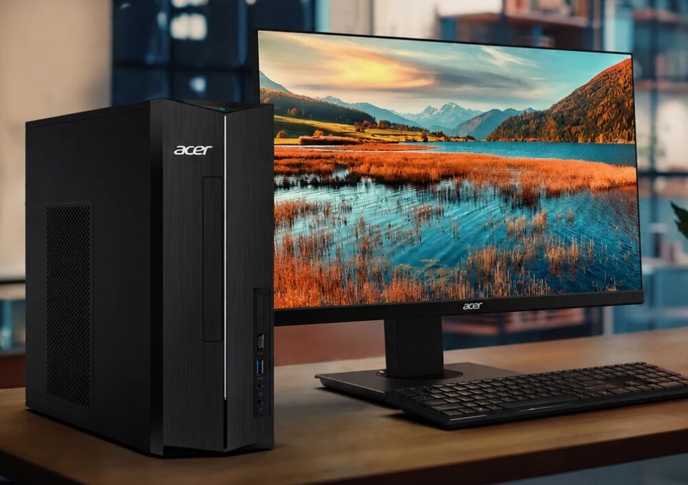 Komputer ACER Aspire XC-1715 TWLD4 Komputer stacjonarny stoi na drewnianym blacie obok monitora z tapetą przedstawiającą górski krajobraz z jeziorem, przed którym leży klawiatura