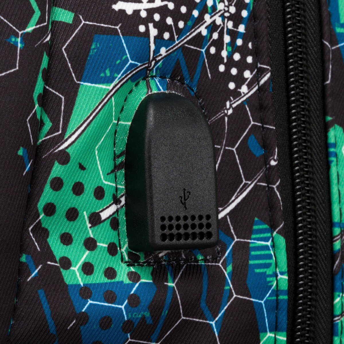 Zbliżenie na fragment plecaka z kolorowym wzorem geometrycznym i portem USB. Wzór zawiera zielone, niebieskie i białe elementy na czarnym tle.
