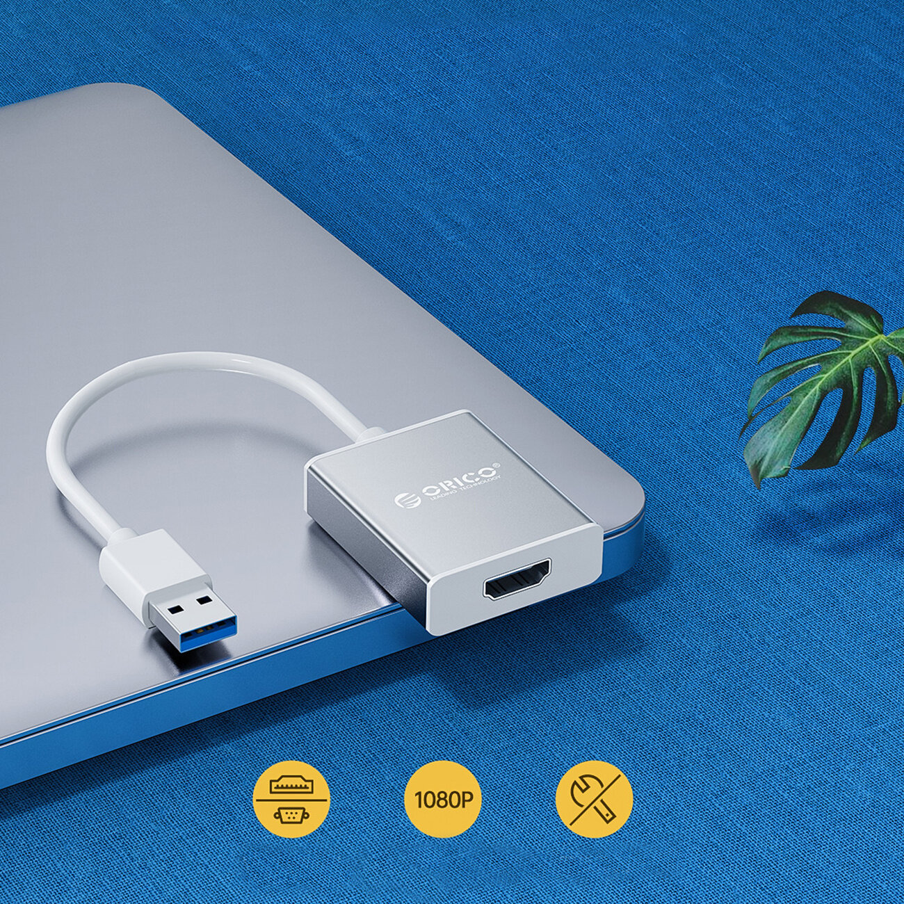 Na obrazie widoczny jest srebrny adapter USB-A 3.0 do HDMI marki Orico, leżący na szarej powierzchni. W dolnej części obrazu znajdują się trzy żółte ikony z symbolami złączy i napisem \'1080P\'.