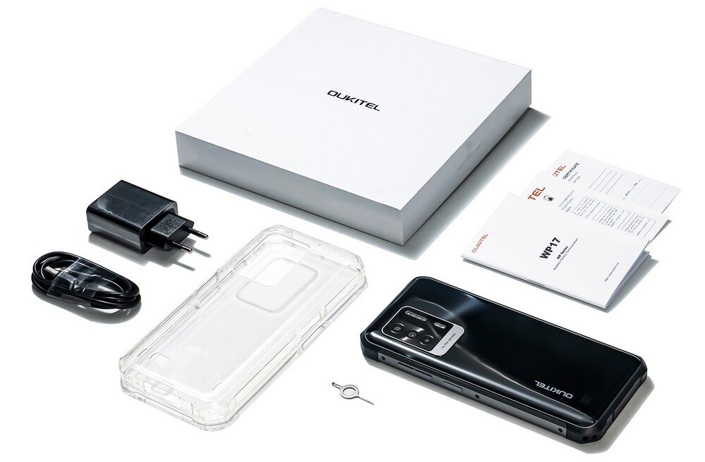 Na obrazie znajduje się zestaw zawierający smartfon, przezroczyste etui, ładowarkę, kabel, narzędzie do wyjmowania karty SIM, instrukcje oraz pudełko z logo \'OUKITEL\'.