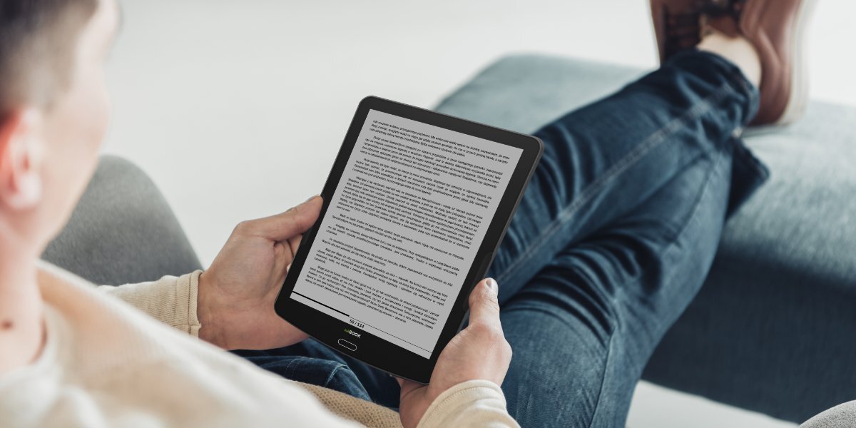 Osoba czytająca książkę na INKBOOK Focus Plus leżąc na kanapie.