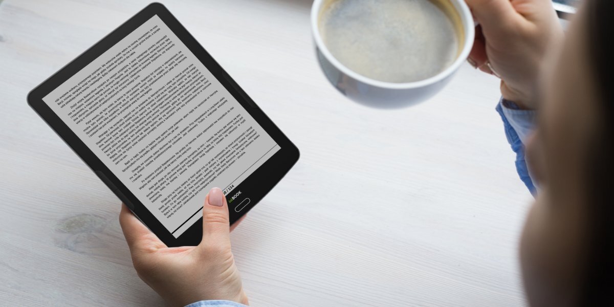 Osoba czytająca książkę na INKBOOK Focus Plus trzymając filiżankę kawy w drugiej dłoni.
