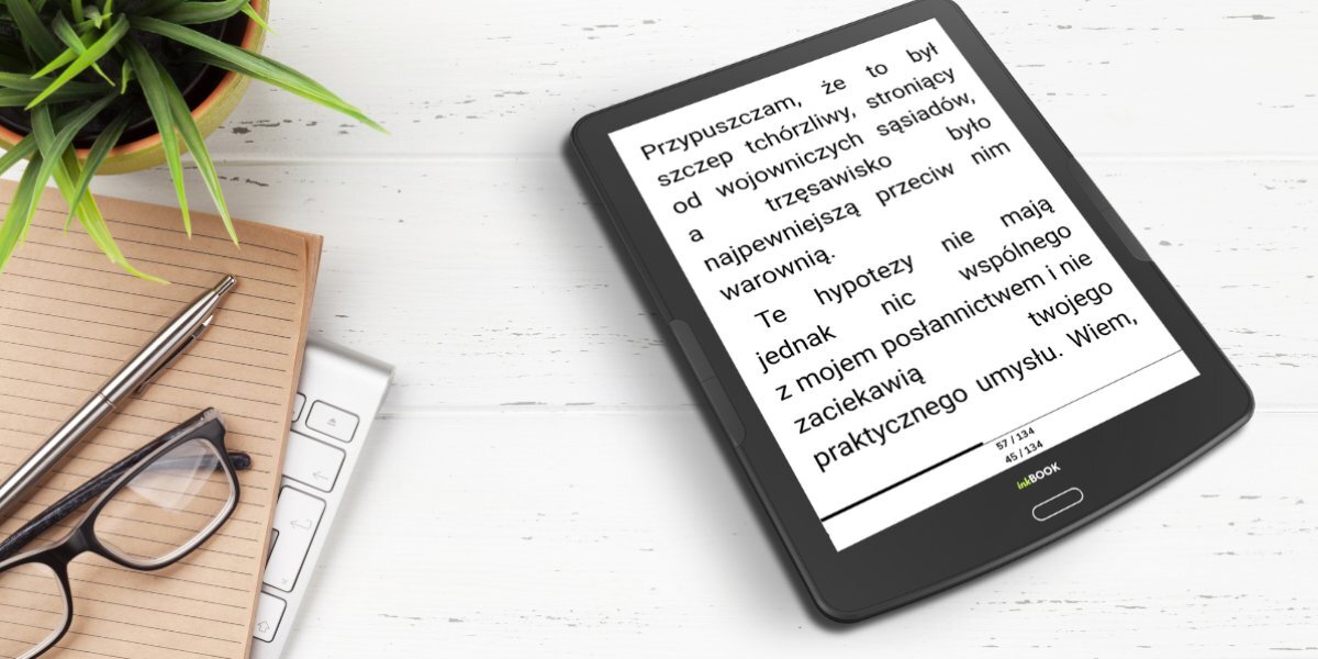 Czytnik ebooków INKBOOK Focus Plus obok notesu, okularów, doniczki z kwiatem oraz długopisu.