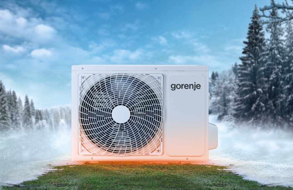 Na obrazie widoczna jest jednostka zewnętrzna klimatyzatora z logo \'gorenje\', umieszczona na tle zimowego krajobrazu z drzewami pokrytymi śniegiem.