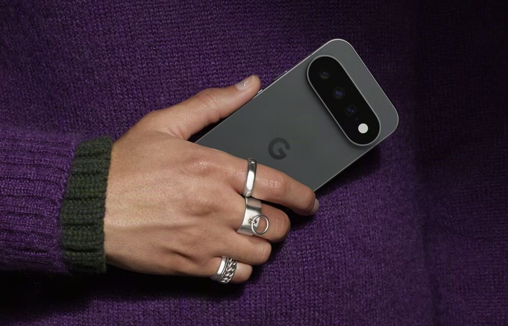 Osoba trzyma smartfon z widocznym logo \'G\' na tylnej obudowie. Telefon ma ciemny kolor i trzy obiektywy aparatu z lampą błyskową.