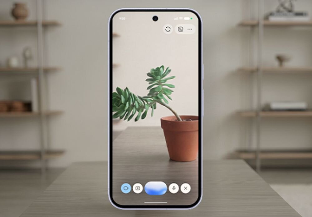 Smartfon z wyświetlaczem pokazującym zdjęcie rośliny w doniczce na stole. W tle widoczne są rozmyte półki z przedmiotami.