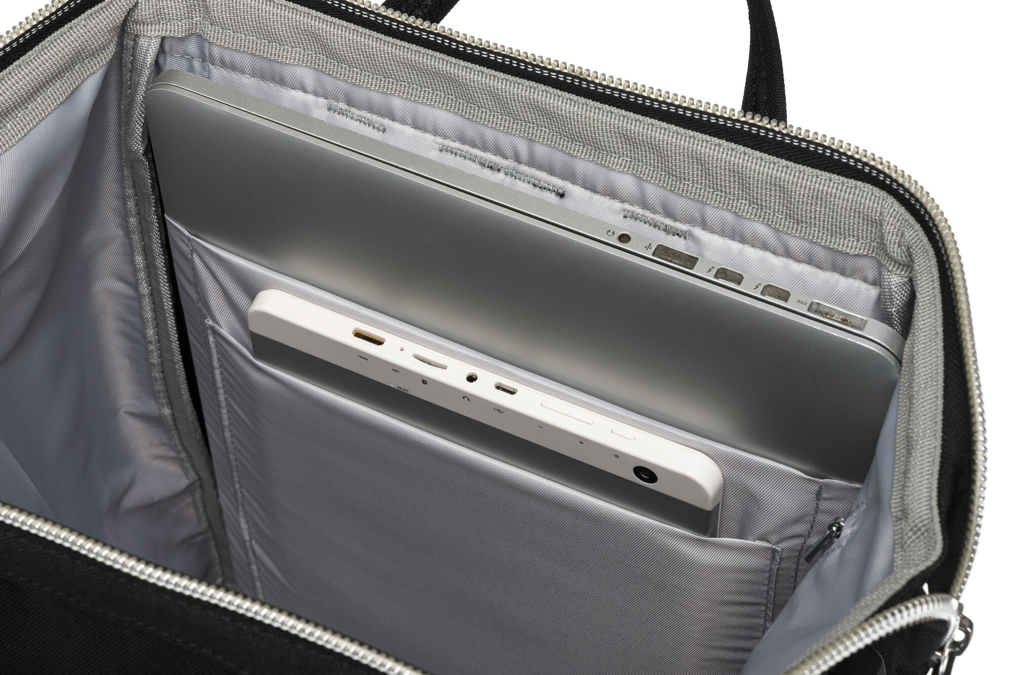 Wnętrze plecaka z szarym wyściełaniem, w którym znajduje się laptop oraz tablet. Widoczne są porty USB i inne złącza na urządzeniach.