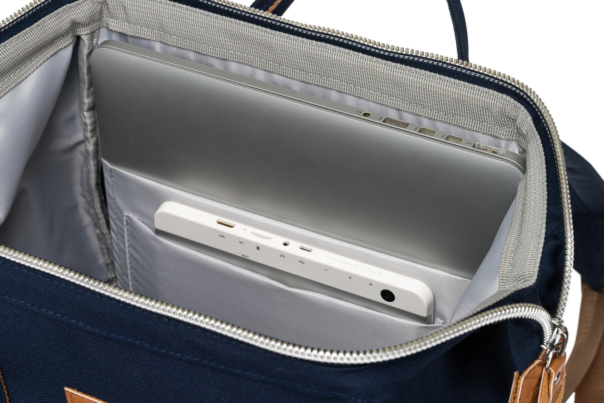 Wnętrze granatowego plecaka z szarym wykończeniem, w którym znajduje się laptop oraz urządzenie z portami USB. Plecak ma zamek błyskawiczny i brązowe uchwyty.