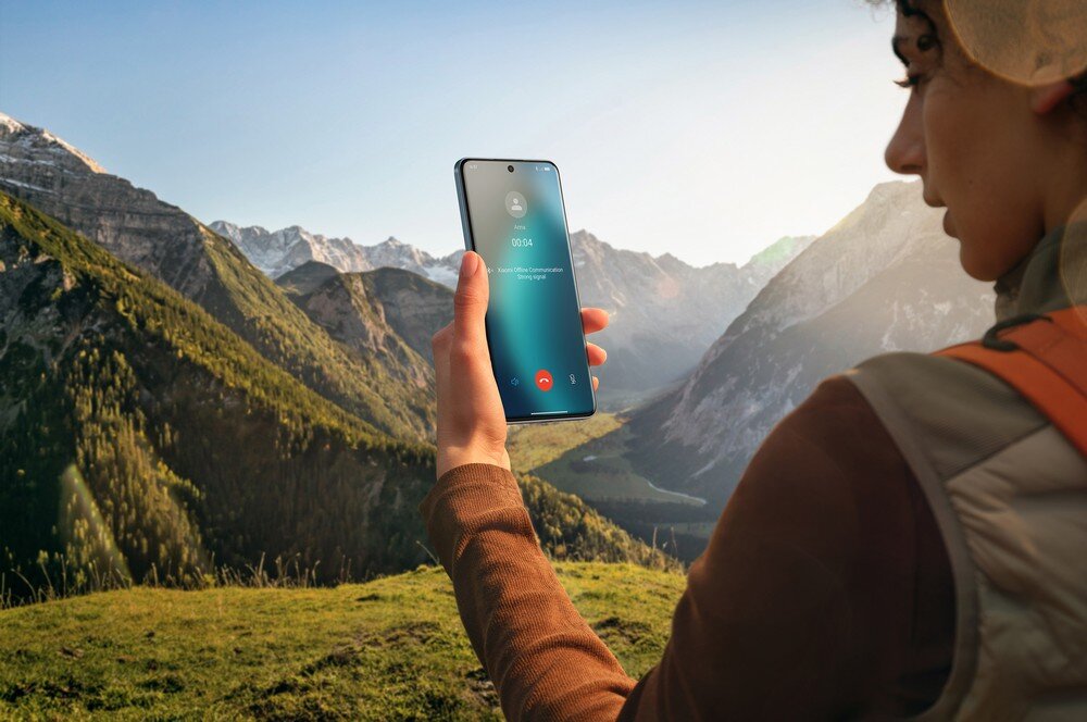 Osoba trzyma smartfon z wyświetlonym ekranem połączenia telefonicznego na tle górskiego krajobrazu. Na ekranie widoczny jest czas trwania połączenia: \'00:34\'.