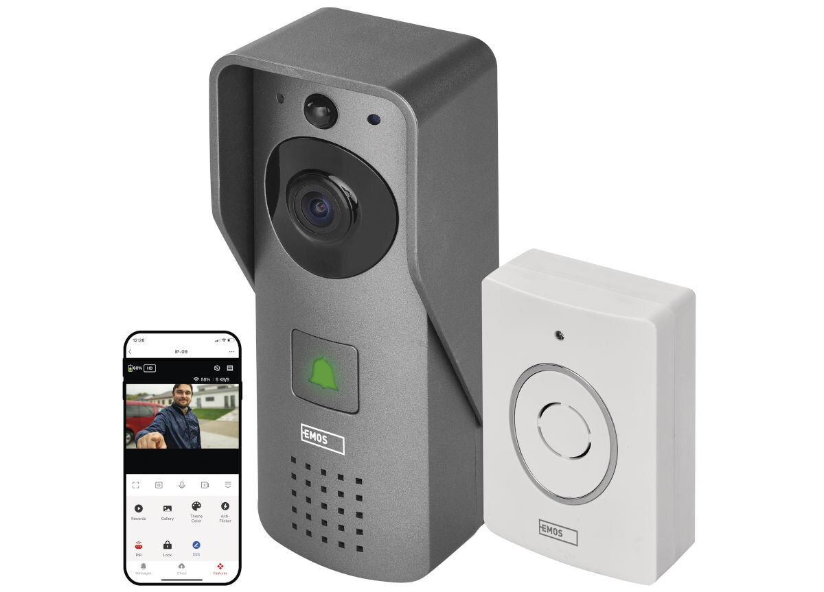 Na obrazie widoczny jest szary dzwonek bezprzewodowy z kamerą i białym przyciskiem, obok znajduje się smartfon z aplikacją pokazującą obraz z kamery. Na dzwonku widnieje logo \'EMOS\'.