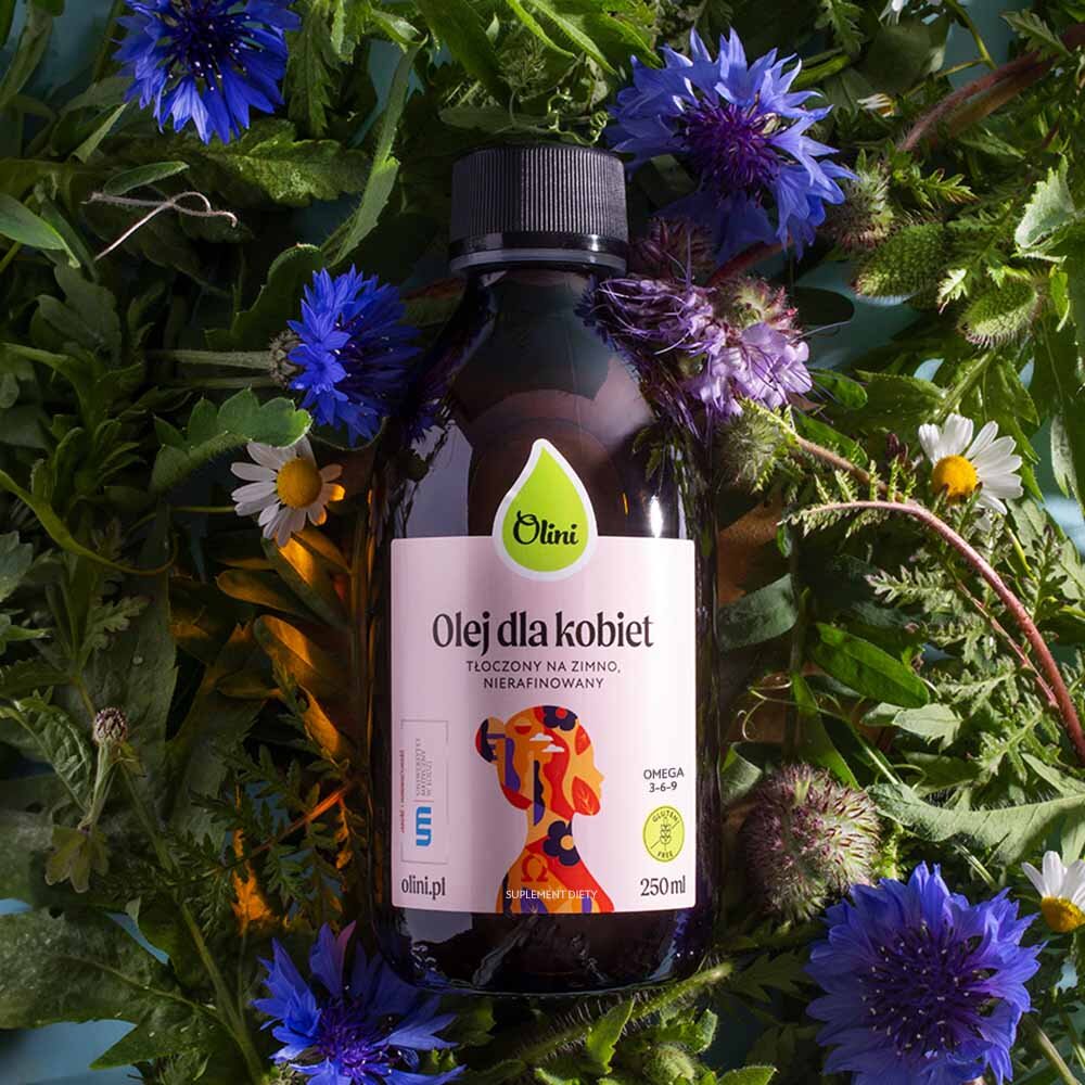 Butelka produktu \'Olini Olej dla Kobiet\' o pojemności 250 ml, otoczona kolorowymi kwiatami i zielonymi liśćmi. Etykieta zawiera napis: \'Olej dla kobiet, tłoczony na zimno, nierafinowany, omega 3-6-9, suplement diety\'.