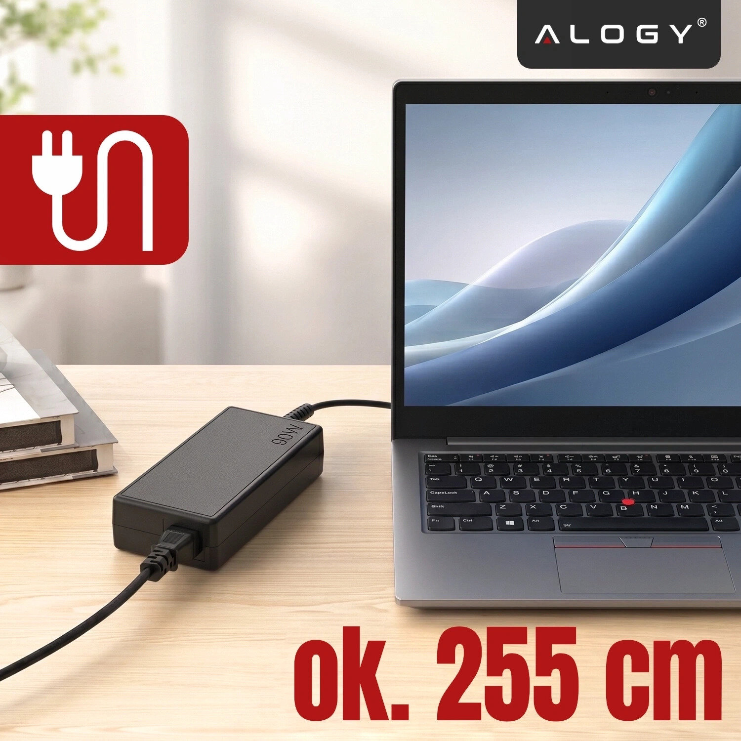 Na drewnianym biurku znajduje się czarny zasilacz podłączony do laptopa, obok widoczne jest logo \'ALOGY\'. Na obrazie widnieje tekst \'ok. 255 cm\' oraz symbol wtyczki na czerwonym tle.