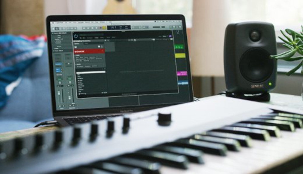Na zdjęciu widać klawiaturę sterującą oraz laptop z otwartym oprogramowaniem muzycznym. Obok znajduje się głośnik z widocznym logo \'GENELEC\'.