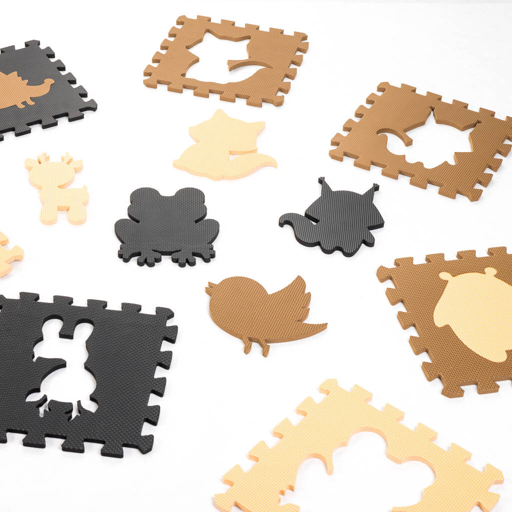 Na obrazie widoczne są elementy piankowej maty edukacyjnej w kształcie puzzli, z wyciętymi sylwetkami zwierząt w kolorach beżowym, brązowym i czarnym. Każdy element ma wycięty kształt, który można dopasować do odpowiedniego otworu.