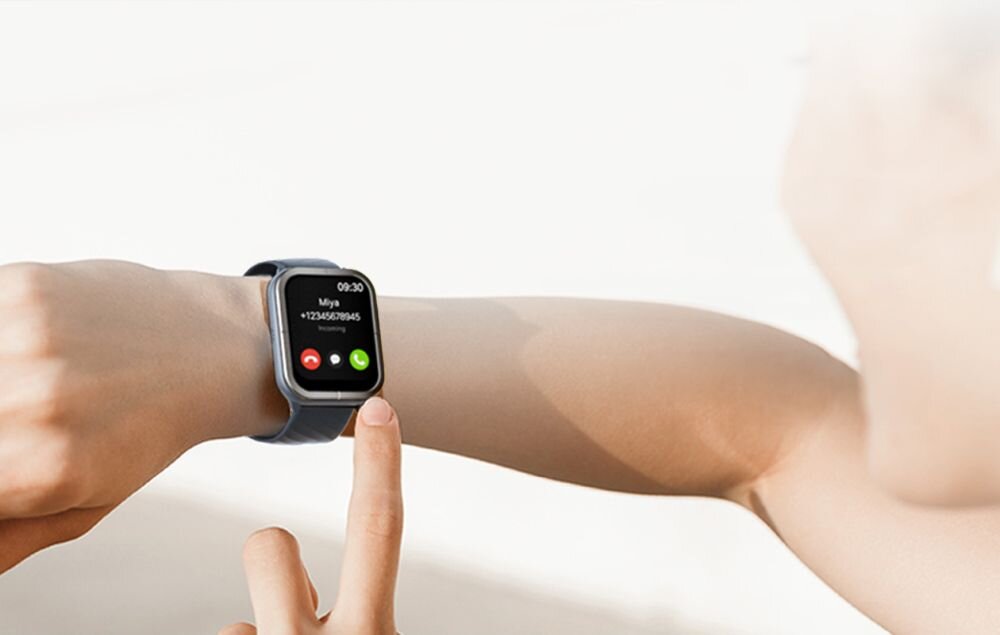 Osoba nosi czarny smartwatch z wyświetlaczem pokazującym połączenie przychodzące od \'Mój\' z numerem +12345678945. Na ekranie widoczne są przyciski do odebrania i odrzucenia połączenia.