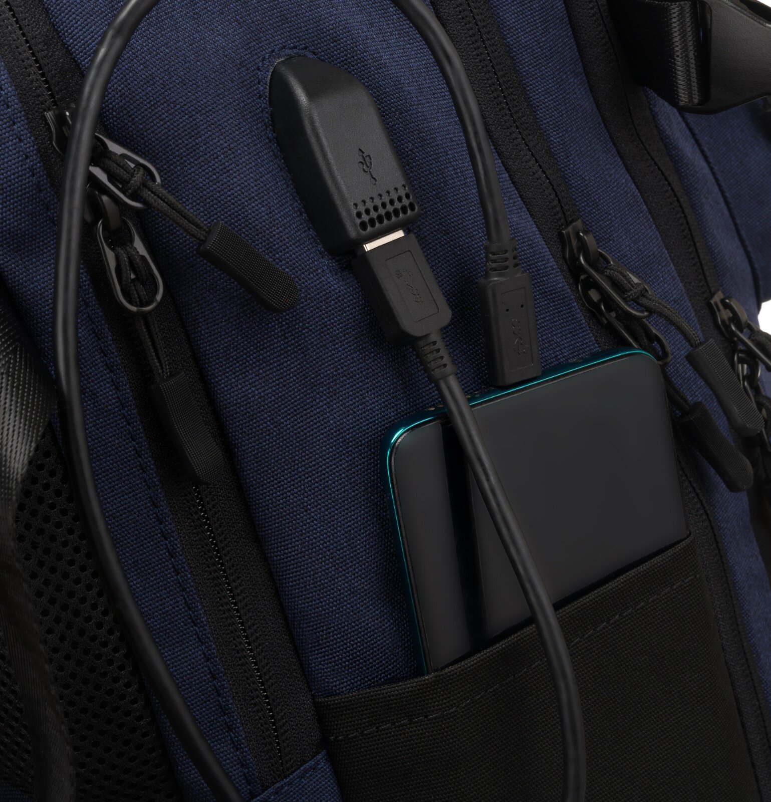 Granatowy plecak z widocznym portem USB i czarnym kablem podłączonym do urządzenia w kieszeni. Plecak ma czarne zamki błyskawiczne i detale z siatki.