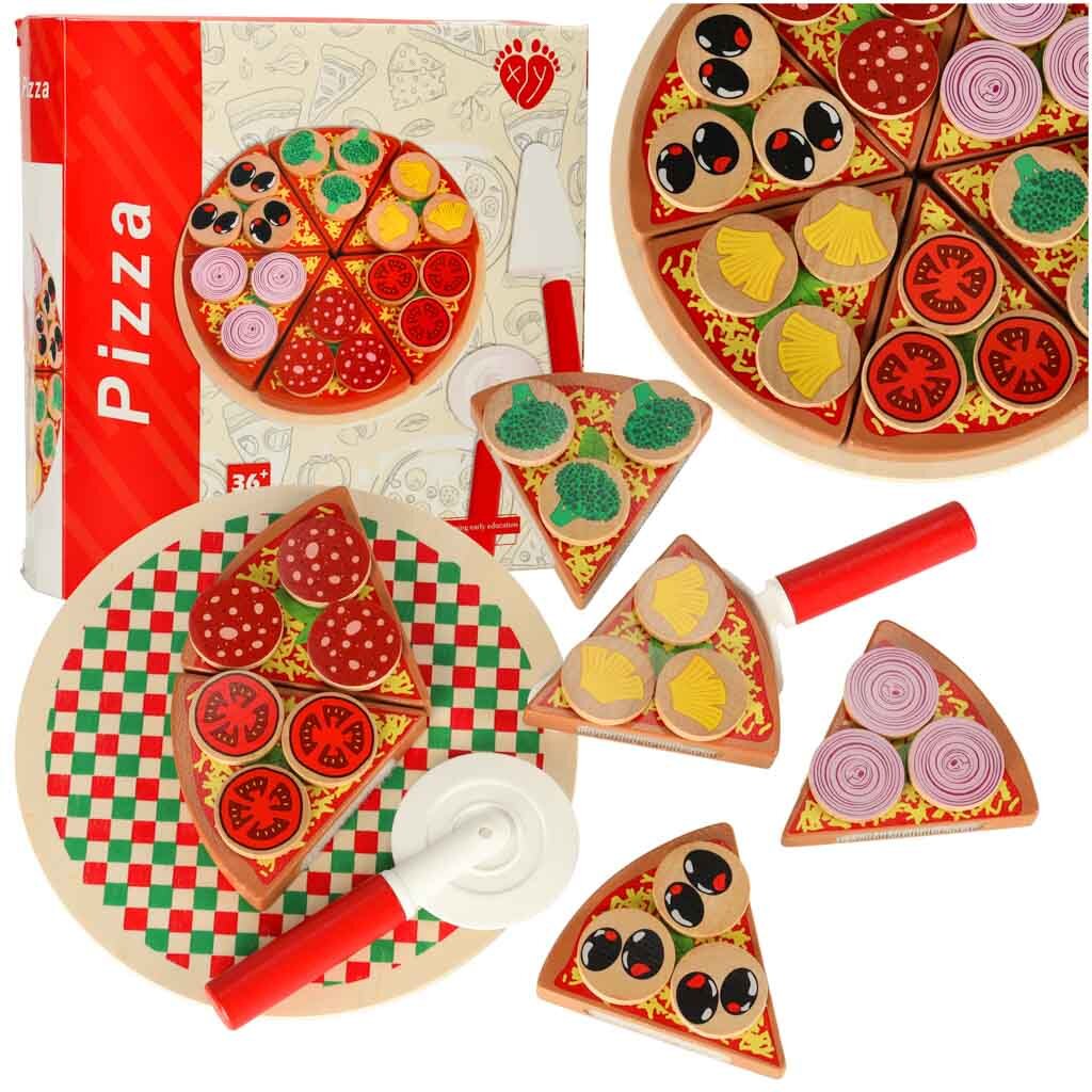 Na obrazie widoczny jest zestaw drewnianej pizzy do krojenia z różnymi dodatkami, w tym kawałki z brokułami, pomidorami, cebulą i oliwkami. Obok znajduje się pudełko z napisem \'Pizza\' oraz plastikowy nóż do krojenia.