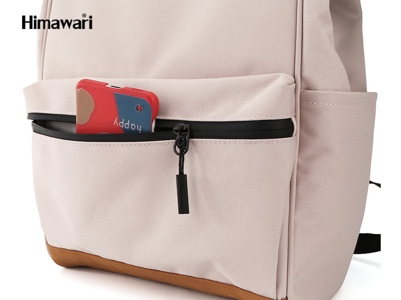 Beżowy plecak z kieszenią zapinaną na czarny zamek błyskawiczny, z wystającym czerwonym etui z napisem \'happy\'. W lewym górnym rogu widoczne jest logo \'Himawari\'.