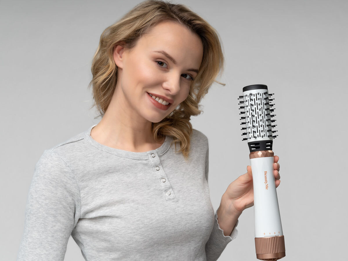 Osoba trzyma suszarko-lokówkę z widocznym napisem \'BEAUTYME\'. Urządzenie ma biały korpus z brązowymi elementami.
