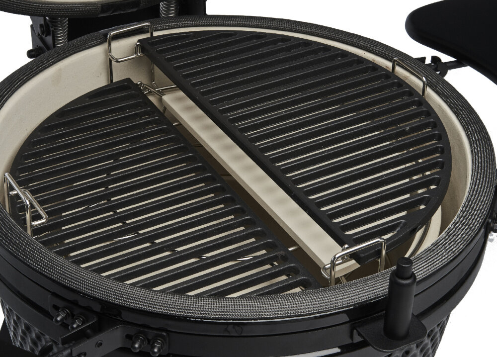 Okrągły grill ceramiczny z czarnym rusztem i białym wnętrzem. Widoczne są metalowe uchwyty i elementy konstrukcyjne.